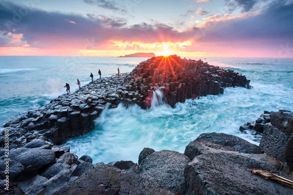 Obraz Fisherman on Giants Causeway at sunrise with red ball of the sun and nice clouds