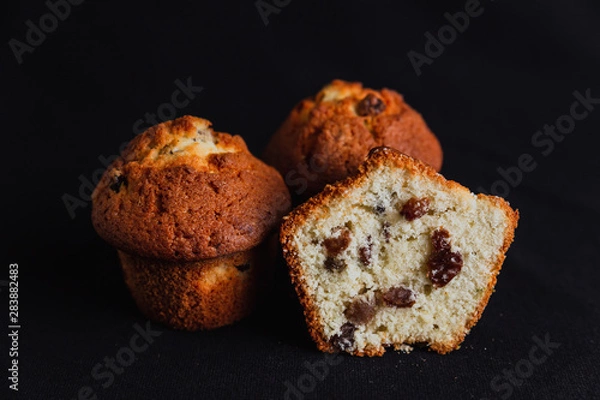 Fototapeta Muffins with raisins and one muffin cut in half on black background
