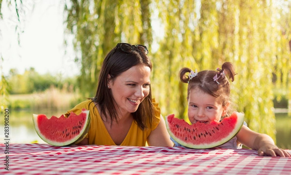 Fototapeta Mother and daughter eating watermelon slice on a picnic In a park