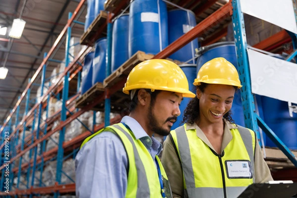Fototapeta Male and female worker discussing on clipboard in warehouse