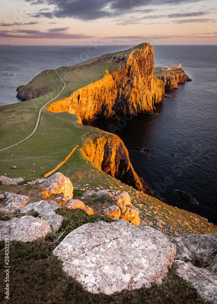 Obraz Neist Point, słynny punkt orientacyjny z latarnią morską na Isle of Skye w Szkocji oświetlony przez zachodzące słońce.