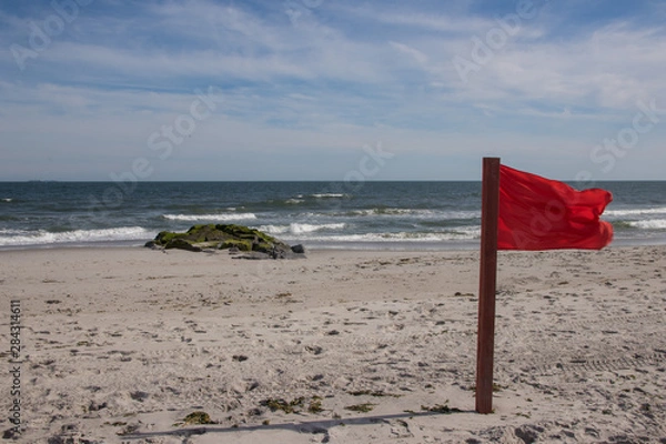 Fototapeta Warning sign of a red flag at a beautiful beach with a blue sky , Long Beach, New York, USA