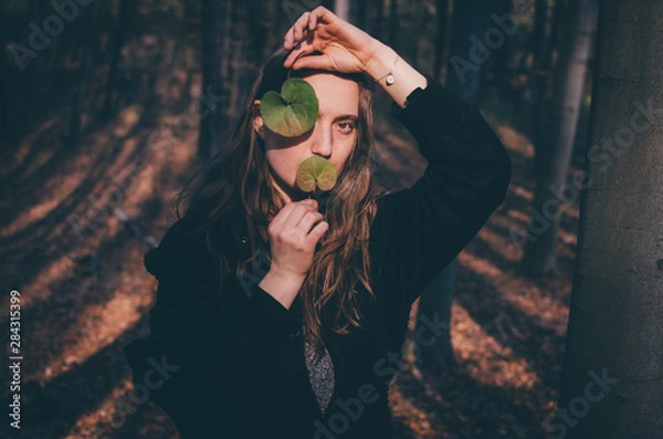Fototapeta Women standing in a autumn park keeps the leave in form of a heart near the face