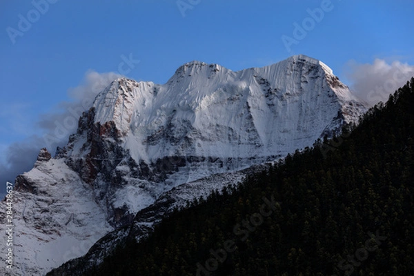 Fototapeta Chenrezig, holy snow mountain in Daocheng Yading Nature Reserve - Garze, Kham Tibetan Pilgrimage region of Sichuan Province China. Snow capped mountain Xiannairi - Dusk, Twilight Blue Sky