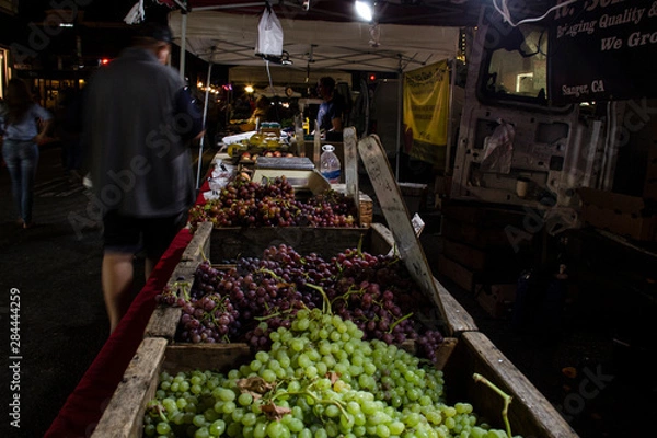 Fototapeta Long table of fruits and vegetables for sale. Lit by LED's to highlight their frshness & color, just after sunset.