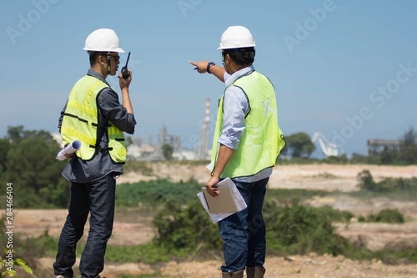 Fototapeta portrait of two engineer's or architect's dress with hardhat safety helmet and safety vest have a meeting and pointing to new construction sites at outdoor