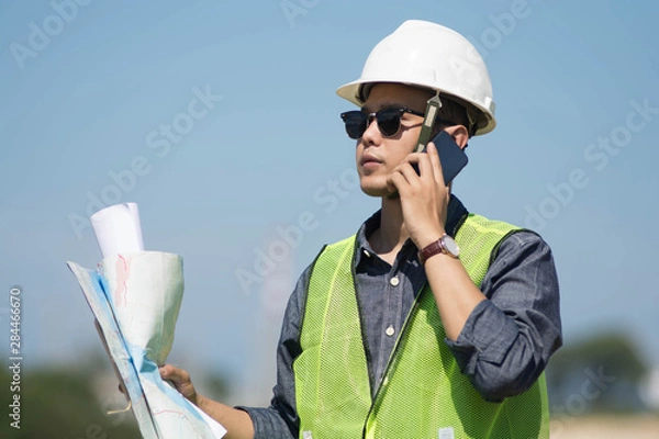Fototapeta portrait of bussy young handsome architect or engineer supervisor talking on cell phone outdoors with clear blue sky