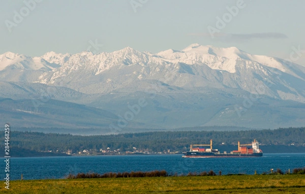Fototapeta USA, WA, Whidbey Island. View from Ebey's Bluff across Strait of Juan de Fuca to Olympic Mountains as container ship makes its way through Puget Sound.