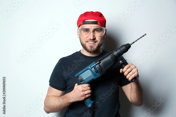 Fototapeta Young working man with rotary hammer on light background