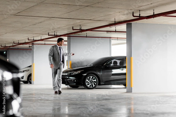 Obraz Quick and comfortable. Businessman in grey suit parks his car at parking lot. Copy space on the right side