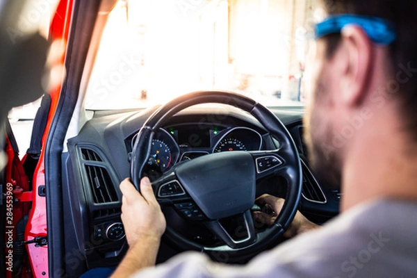 Fototapeta Technician with safety glasses starting the engine of a car during a vehicle inspection