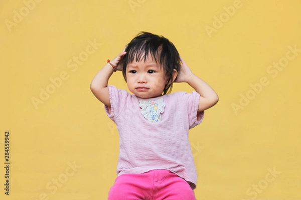 Fototapeta Soft focus. Portrait image of 1-2 years old of Asian baby child girl put her hand on her head and scratching hairs. She crying and sad. Expression and emotions of kid concept.