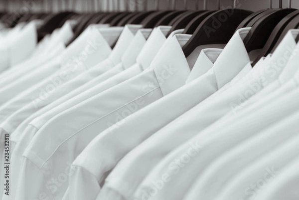 Obraz Row of white shirts hang on black hangers on a rack in a shop. A close-up.