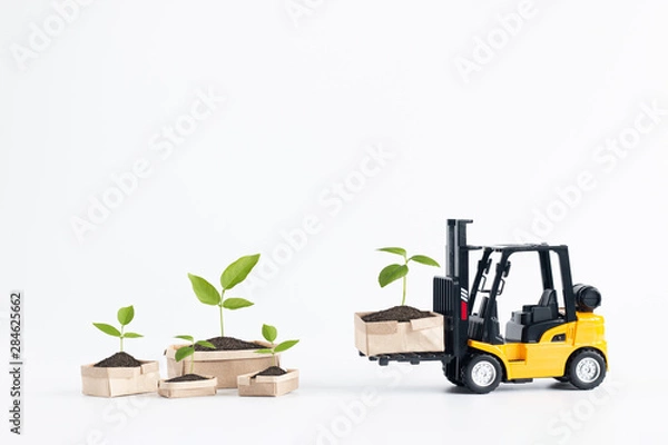 Fototapeta Miniature  forklift truck model loading cardboard boxes containing young plant isolated on white background with copy space for text message