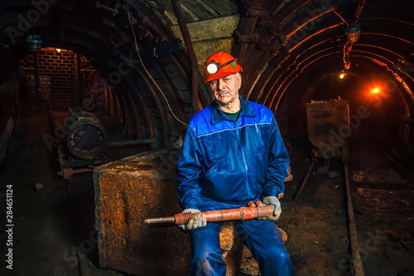 Fototapeta A miner in a coal mine stands near a trolley. Copy space.
