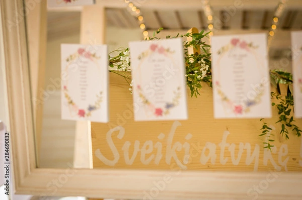 Fototapeta Wedding table sitting chart on cards attached to a mirror and reflection of green leaves