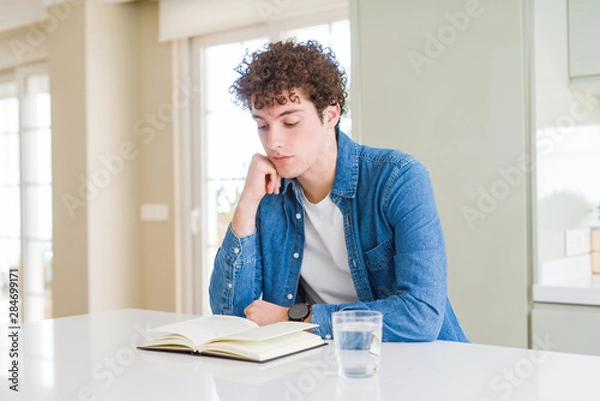 Fototapeta Young man reading a book at home serious face thinking about question, very confused idea