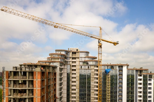 Fototapeta Apartment or office tall building under construction. Brick walls, glass windows, scaffolding and concrete support pillars. Tower crane on bright blue sky copy space background.