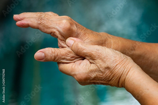 Fototapeta Trigger Finger, Senior woman's left hand massaging her thumb finger, Suffering from pain, Close up and macro shot, Swimming pool background, Health care concept