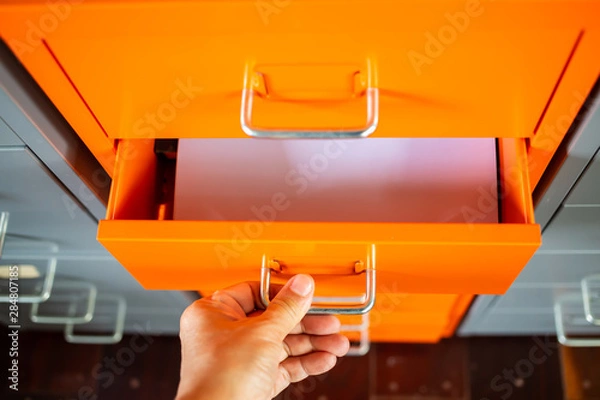 Fototapeta Woman's hand opening drawer of orange metal colour  filing cabinet, White papers for write letter, Administration and storage, Close up shot, Selective focus, Stationery, Business concept