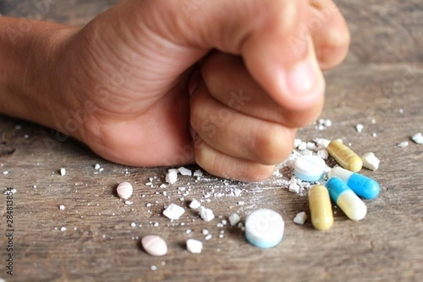 Fototapeta Hands clenched on a multicolored drug placed on a wooden table