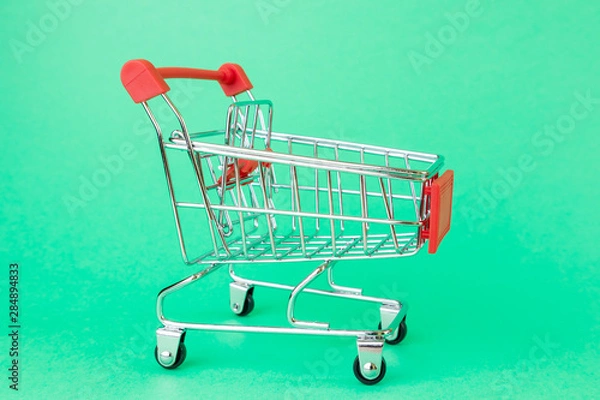 Fototapeta Reduced copy of a shopping cart for supermarkets on a green background. The concept of shopping, grocery shopping, discounts, promotions. Minimalism, place for text.