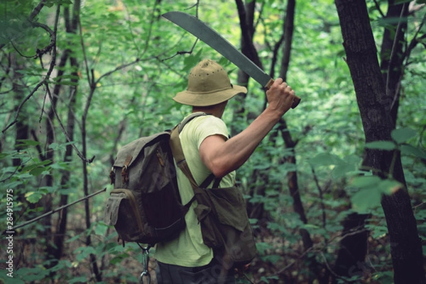 Fototapeta Tourist clears his way with a machete.