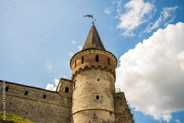 Fototapeta ancient medieval castle tower and stone wall on blue sky with white clouds background, copy space 
