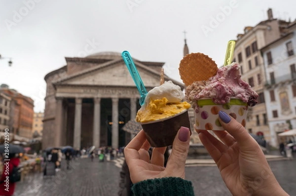 Fototapeta Two glasses of Italian ice cream in the hands of a girl against the Roman Pantheon in Piazza della Rotonda in Italy on a rainy day