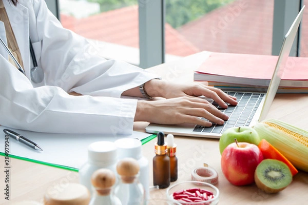 Fototapeta close up photo of Young Asian female nutritionist doctor work on laptop at wooden table with fresh fruit and medicine on foreground in laboratory, healthy concept