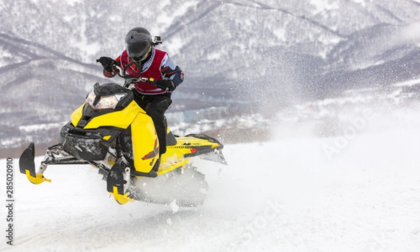 Fototapeta man is flying on a snowmobile on a background mountains