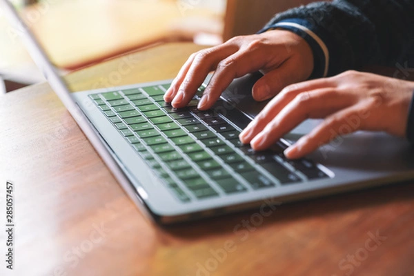 Fototapeta Closeup image of hands using and typing on laptop computer keyboard on the table