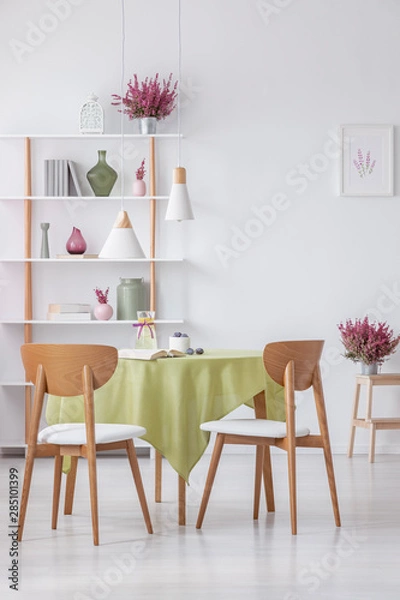 Fototapeta Chairs at table in elegant dining room with heather in pots and accessories on shelf , real photo