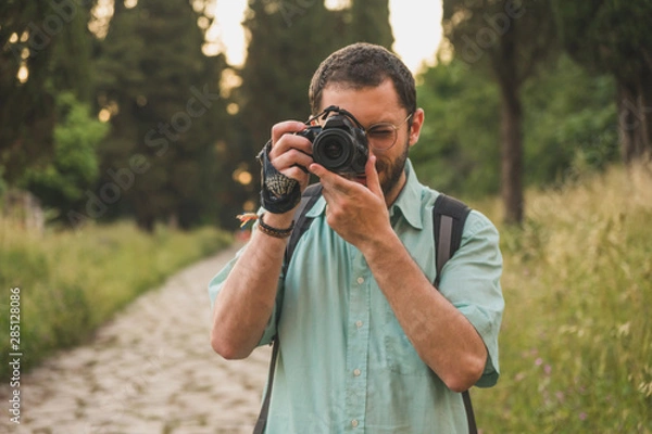 Fototapeta Young photographer focusing and taking a picture towards the camera in the middle of the nature