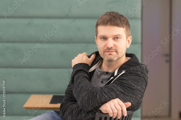 Obraz Photo shoot in cafe. Determined man. Man sitting, looking at the camera, right. On a chair, half turned.