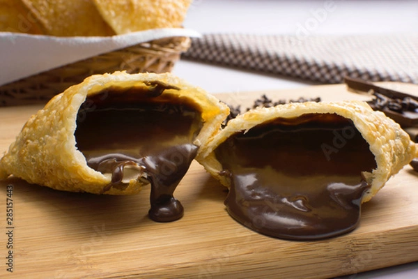 Obraz One open tradional Brazilian fried pastry called pastel stuffed with chocolate Brazilian dessert brigadeiro in a cutting board with half light