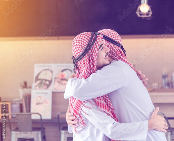 Obraz Two Arabian men who are friends together are hugging and smiling when they accidentally meet each other at the cafe & restaurant in the morning