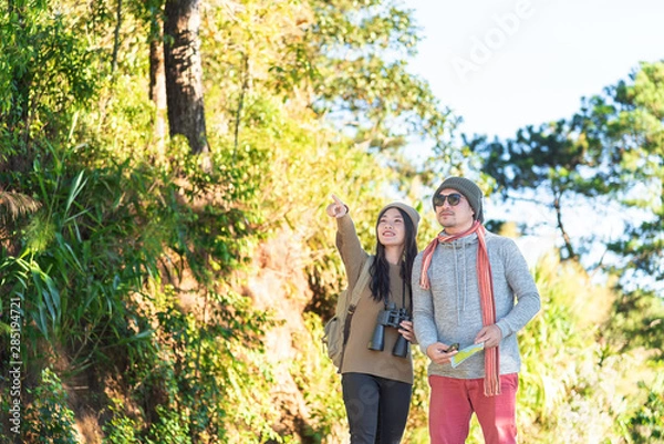 Obraz woman who is holding a binoculars points to something for the man who is her boyfriend while they are traveling into the wild in the morning on vacation