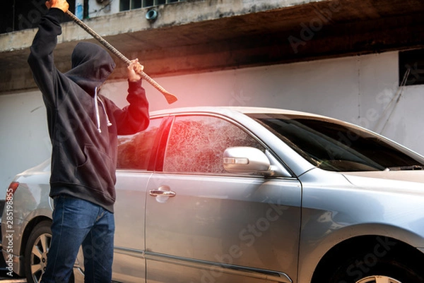 Obraz Car thief stealing to break glass into a car .Masked hide face man ,robber dressed in black holding crowbar into car damage glass window of car.
