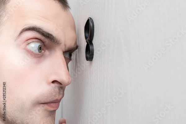 Fototapeta Man look out through the peephole of front door, portrait, closeup, toned
