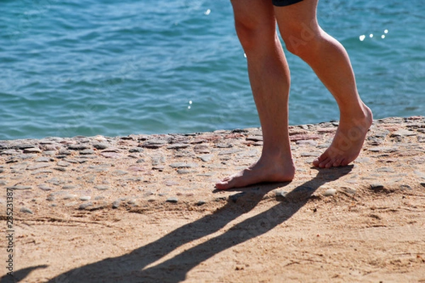 Fototapeta Man legs on sand. Male feet walking on beautiful sandy beach of hotel resort on Red sea in Egypt, doing and leave behind footprints in sand. Man on vacation in summertime. Travel and holiday concept.