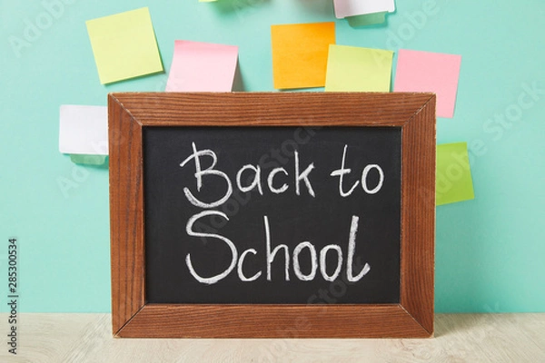 Fototapeta chalkboard with back to school lettering near multicolored sticky notes on turquoise wall
