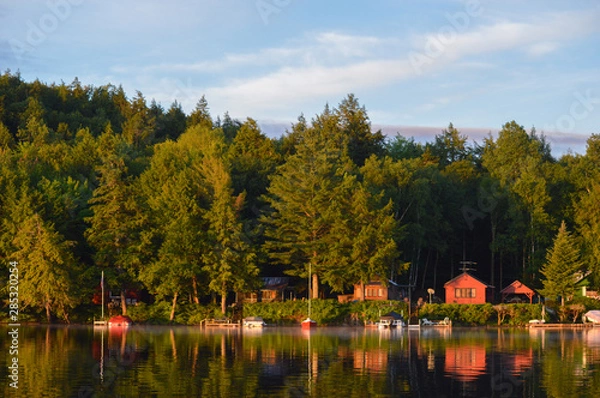 Obraz Cabin coastline on Saranac Lake in upstate New York bathed in the morning sunrise. The colored cabins are reflected in the water