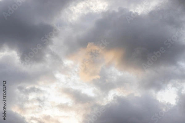 Fototapeta Dark rain clouds. On the clouds you can see a yellow spot from the sunlight. The sun is shining behind the clouds. Overcast weather. Background with free space and empty place.