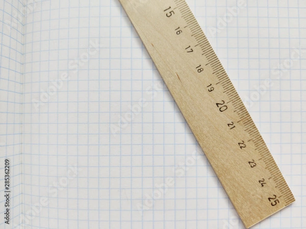Obraz Wooden ruler with metric system rests on a white checkered exercise book without notes. School notebook in a cage. Empty notepad with square texture. Measuring ruler