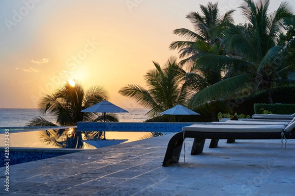Obraz Blue and orange sky morning sunrise on beach with swimming pool and palm trees in the dominican republic tropical island