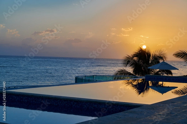 Obraz Blue and orange sky morning sunrise on beach with swimming pool and palm trees in the dominican republic tropical island
