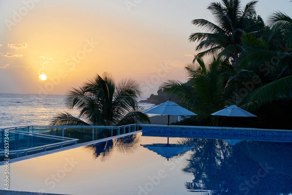 Obraz Blue and orange sky morning sunrise on beach with swimming pool and palm trees in the dominican republic tropical island