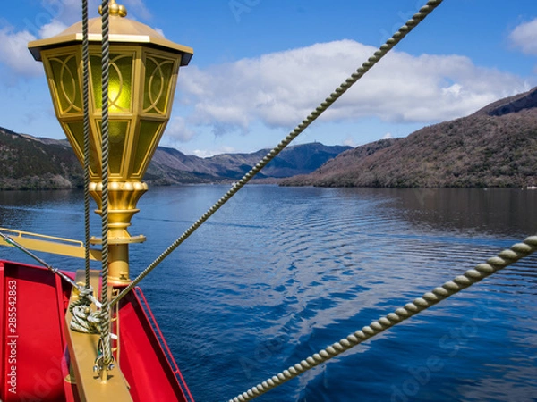 Obraz Lake and forests in Japan - picture taken from a boat on the lake, decorative gold coloured lantern, red hull and several lines of ropes in foreground