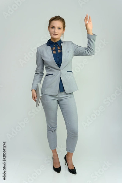 Fototapeta Full length studio portrait of a pretty young woman girl in a business suit on a white background with a folder in hands. He stands right in front of the camera, explains, with emotion.